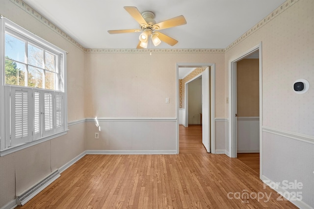 unfurnished room with a ceiling fan, baseboards, light wood finished floors, wallpapered walls, and a baseboard heating unit