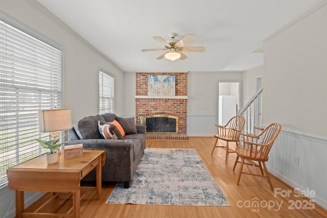 living room with ornamental molding, a brick fireplace, a ceiling fan, and wood finished floors