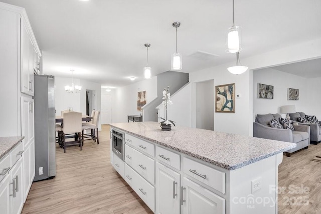 kitchen with light wood finished floors, a center island, light stone counters, freestanding refrigerator, and white cabinets