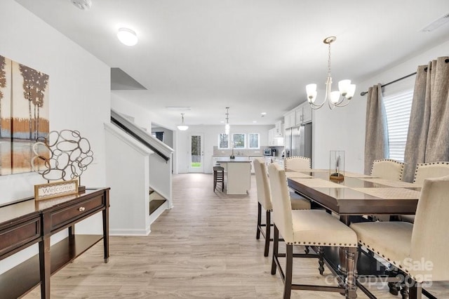 dining area featuring light wood finished floors, stairway, and an inviting chandelier