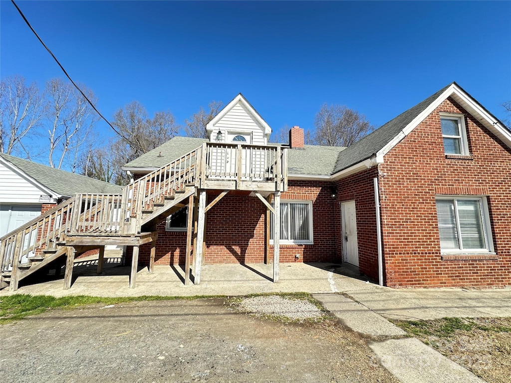 view of front facade with brick siding, stairway, roof with shingles, a chimney, and a deck