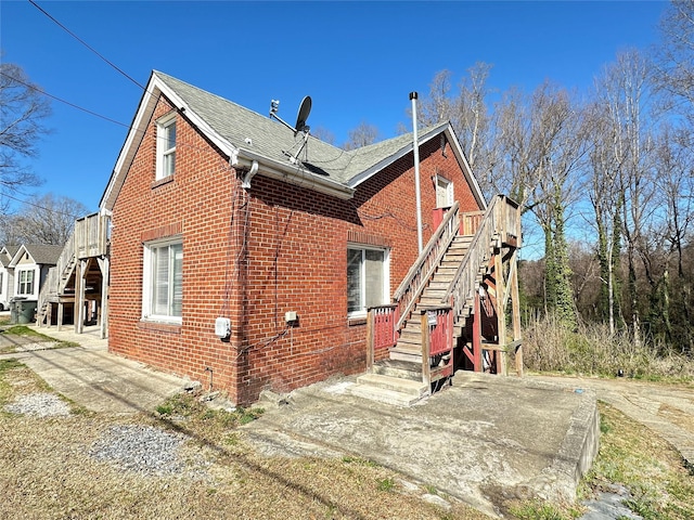 view of home's exterior with stairway, brick siding, and a shingled roof