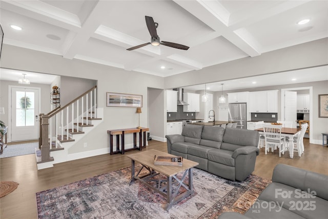 living area with baseboards, coffered ceiling, wood finished floors, and stairs