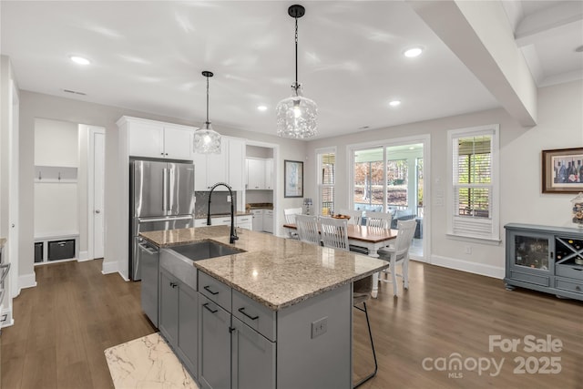 kitchen with light stone counters, a sink, white cabinetry, stainless steel appliances, and dark wood-style flooring