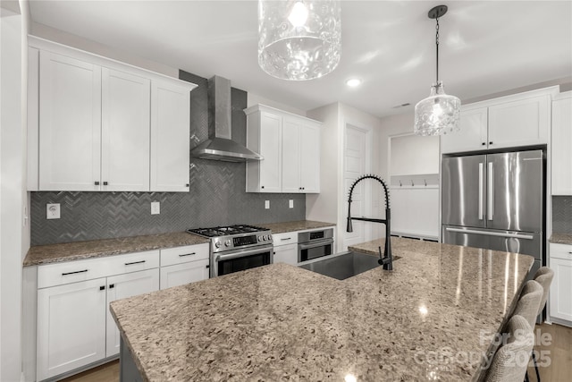 kitchen featuring backsplash, wall chimney range hood, an island with sink, appliances with stainless steel finishes, and a sink