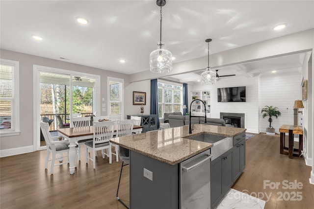 kitchen featuring a center island with sink, dark wood-style flooring, a sink, open floor plan, and a large fireplace