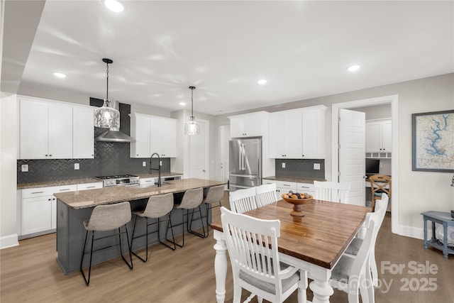 kitchen featuring a center island with sink, freestanding refrigerator, stove, wall chimney exhaust hood, and a sink