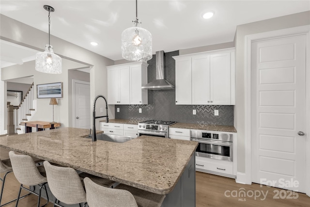 kitchen featuring a sink, stainless steel appliances, a breakfast bar area, wall chimney exhaust hood, and white cabinets