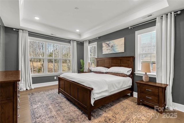 bedroom featuring multiple windows, a raised ceiling, and light wood-style flooring