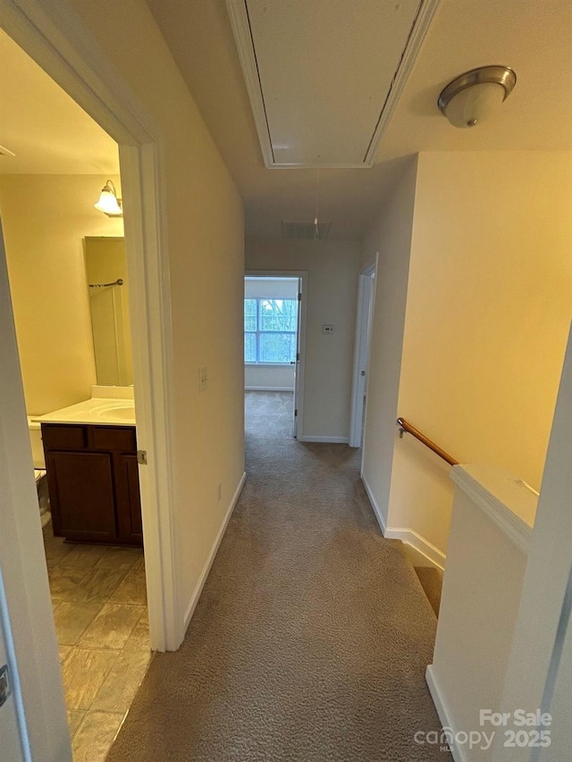 hall with baseboards, light carpet, and attic access