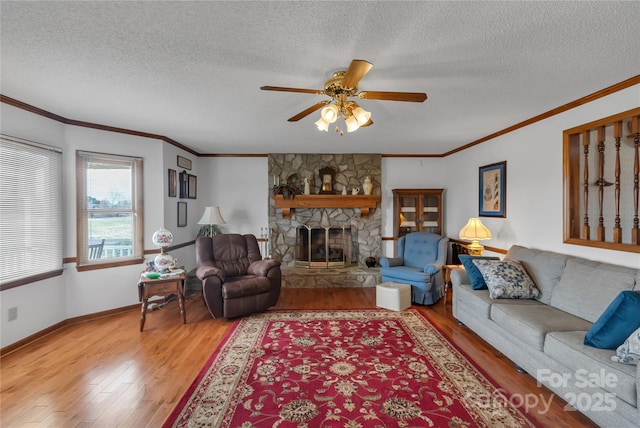 living room with a fireplace, crown molding, light wood-style floors, and a ceiling fan