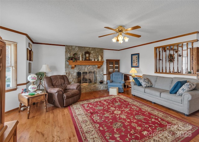 living room featuring a fireplace, ornamental molding, ceiling fan, light wood-style floors, and a textured ceiling