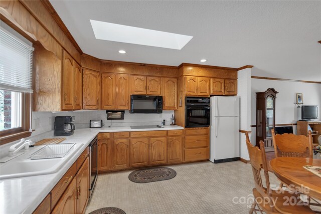 kitchen featuring light countertops, a skylight, brown cabinetry, black appliances, and a sink