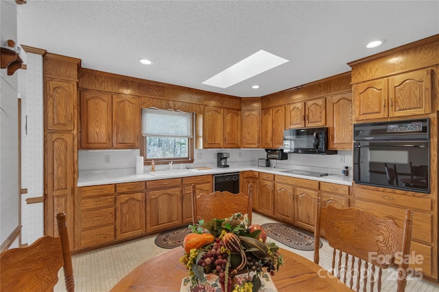 kitchen featuring a sink, black appliances, a skylight, and light countertops