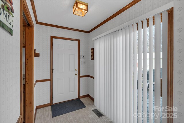 foyer entrance featuring visible vents, wallpapered walls, baseboards, and ornamental molding