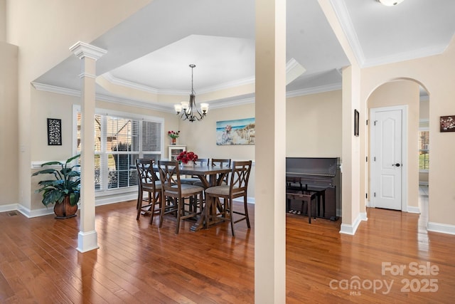 dining room featuring crown molding, baseboards, hardwood / wood-style flooring, arched walkways, and ornate columns