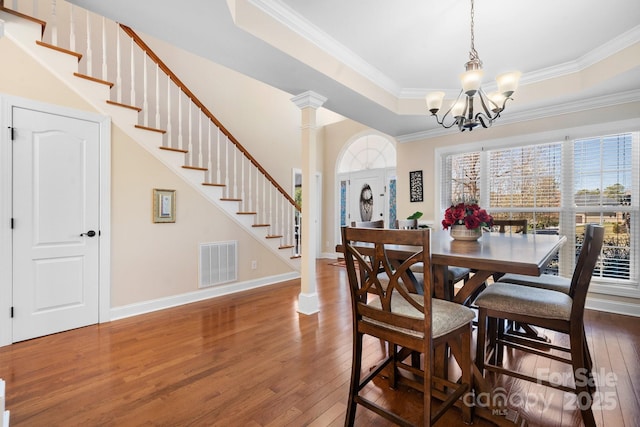 dining room featuring hardwood / wood-style floors, visible vents, a tray ceiling, decorative columns, and stairs