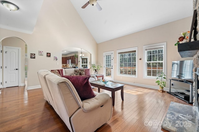 living room featuring baseboards, hardwood / wood-style floors, ceiling fan with notable chandelier, arched walkways, and high vaulted ceiling