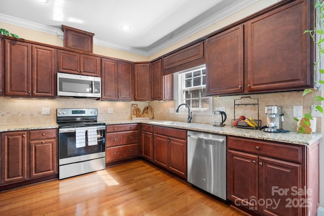 kitchen with a sink, tasteful backsplash, appliances with stainless steel finishes, crown molding, and light wood finished floors