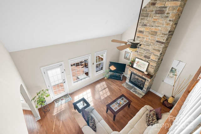 living area featuring a stone fireplace, wood finished floors, baseboards, and vaulted ceiling