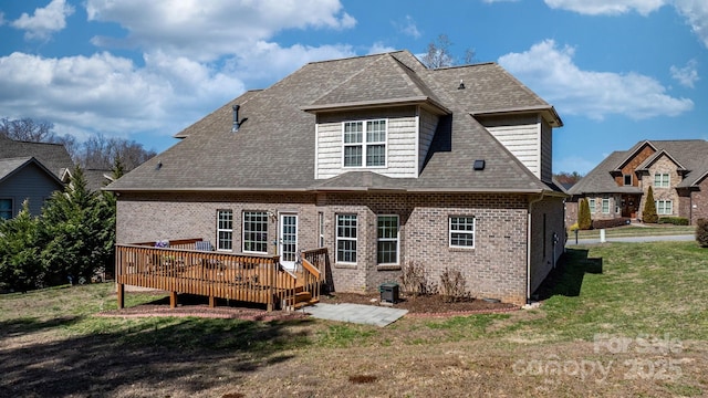 back of property with a yard, brick siding, roof with shingles, and a wooden deck