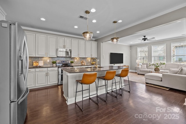 kitchen featuring tasteful backsplash, open floor plan, a breakfast bar, stainless steel appliances, and a sink