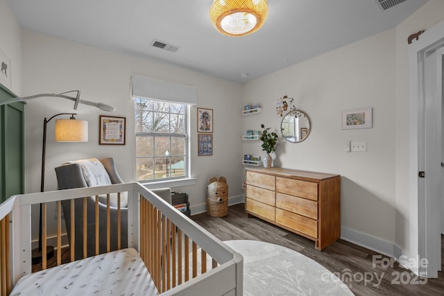 bedroom with a crib, wood finished floors, visible vents, and baseboards