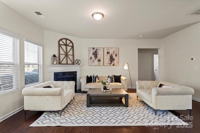 living room with visible vents, baseboards, a glass covered fireplace, and wood finished floors