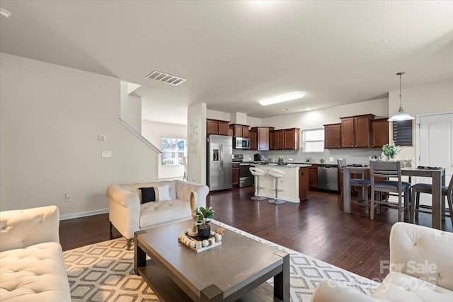 living room featuring dark wood-style floors, a healthy amount of sunlight, visible vents, and baseboards