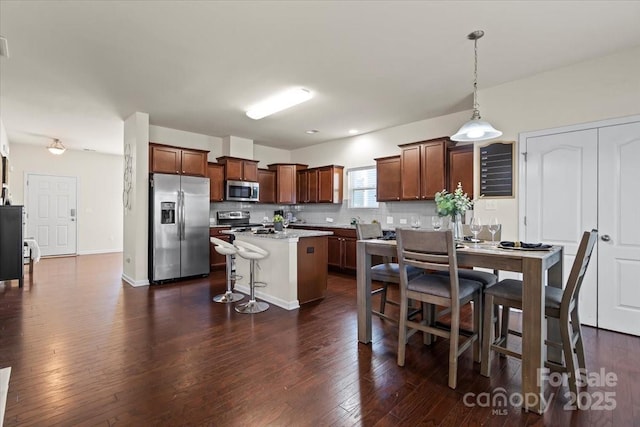 kitchen featuring a kitchen breakfast bar, dark wood-style floors, tasteful backsplash, and appliances with stainless steel finishes