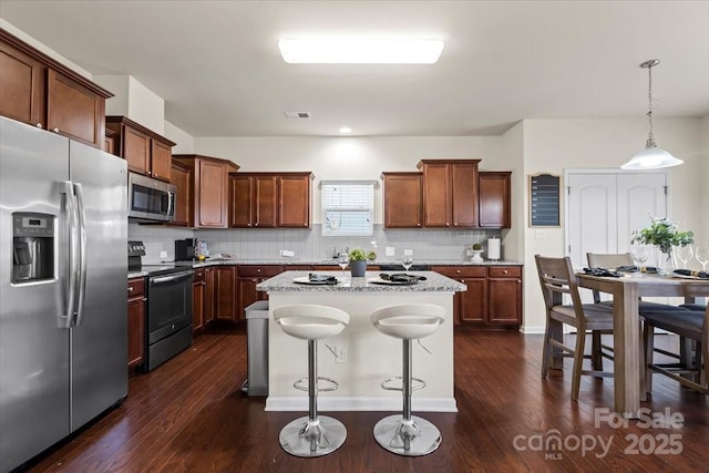 kitchen with stainless steel appliances, decorative backsplash, a breakfast bar area, and dark wood-style flooring