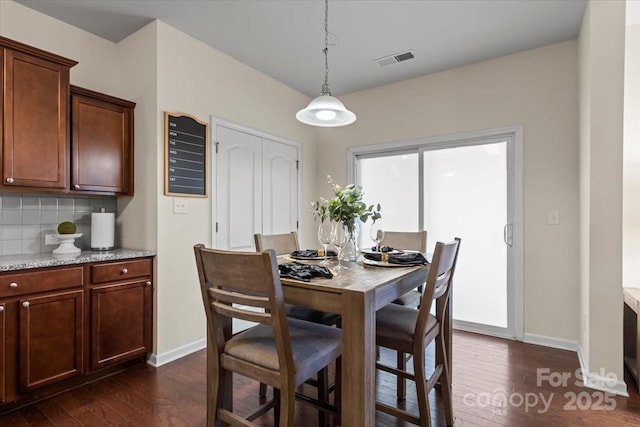 dining room with dark wood finished floors, visible vents, and baseboards