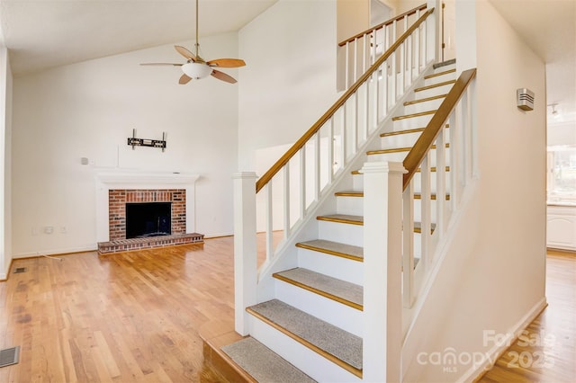 stairway featuring visible vents, ceiling fan, a fireplace, wood finished floors, and high vaulted ceiling