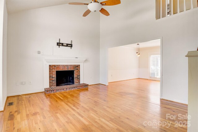 unfurnished living room featuring a fireplace, a ceiling fan, visible vents, a high ceiling, and wood finished floors