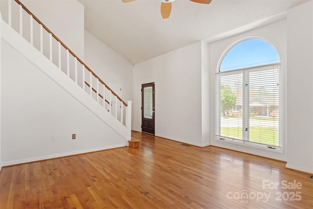 unfurnished living room with high vaulted ceiling, stairway, ceiling fan, and wood finished floors