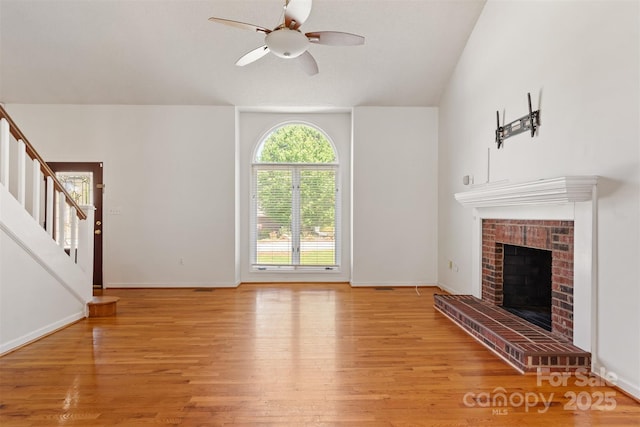 unfurnished living room featuring baseboards, a brick fireplace, ceiling fan, light wood-type flooring, and stairs
