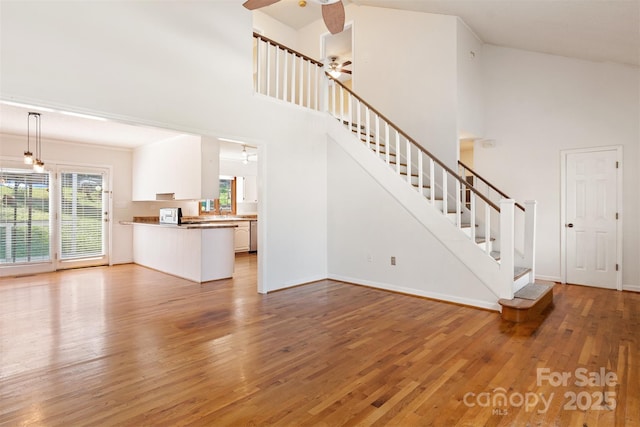 unfurnished living room with baseboards, ceiling fan, light wood finished floors, stairs, and high vaulted ceiling
