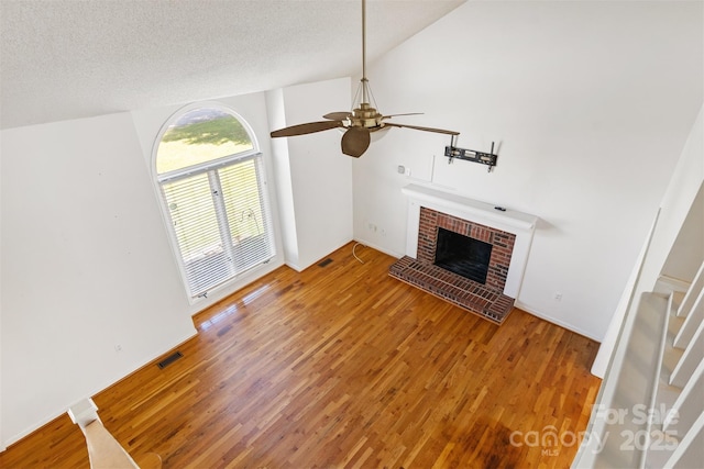 unfurnished living room with light wood-type flooring, a textured ceiling, a ceiling fan, a brick fireplace, and visible vents