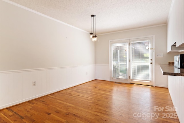unfurnished dining area featuring light wood-style floors, a textured ceiling, ornamental molding, and visible vents