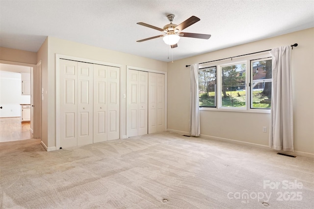 unfurnished bedroom featuring visible vents, baseboards, a ceiling fan, multiple closets, and carpet flooring