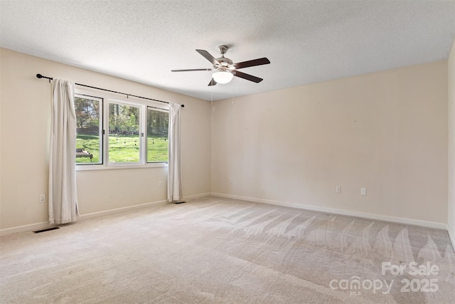 carpeted spare room with a textured ceiling, ceiling fan, baseboards, and visible vents