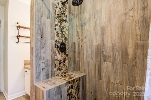bathroom featuring a tile shower, vanity, wood finished floors, and baseboards