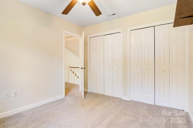 unfurnished bedroom featuring two closets, carpet, a ceiling fan, visible vents, and baseboards