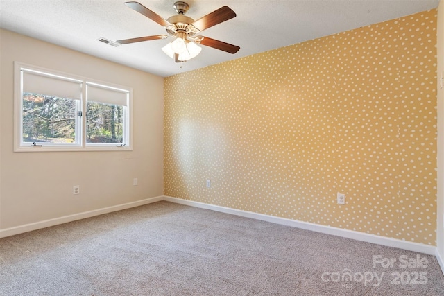 carpeted spare room with visible vents, baseboards, and a ceiling fan