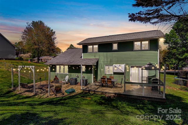 back of property with a yard, fence, central air condition unit, a wooden deck, and roof with shingles