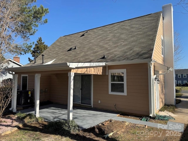 rear view of property featuring cooling unit, a patio, roof with shingles, and a chimney