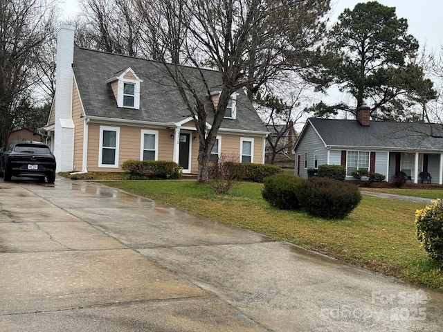 cape cod house featuring driveway, a chimney, and a front lawn