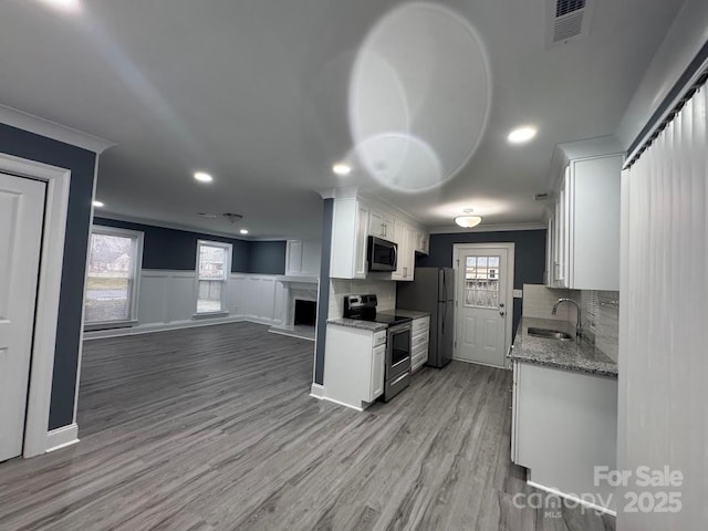 kitchen featuring a sink, ornamental molding, stainless steel appliances, white cabinetry, and open floor plan