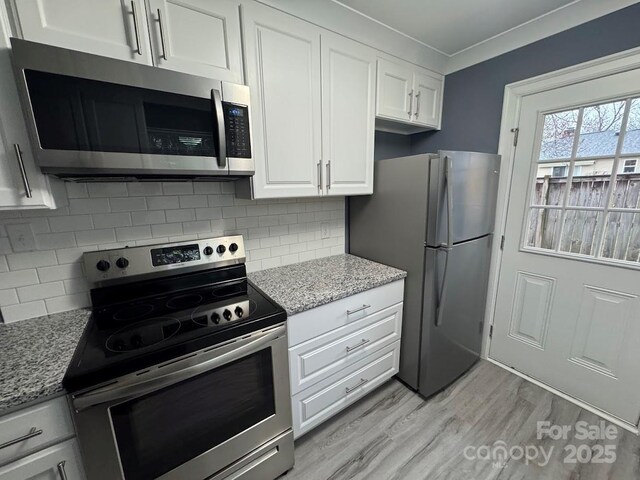 kitchen with white cabinets, light stone counters, light wood-style flooring, and stainless steel appliances