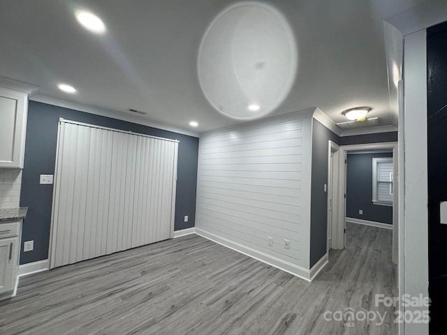 spare room featuring baseboards, crown molding, and light wood finished floors